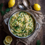 Lemon herb spring vegetable orzo with zucchini, fresh herbs, and lemon zest in a serving bowl on a rustic wooden table