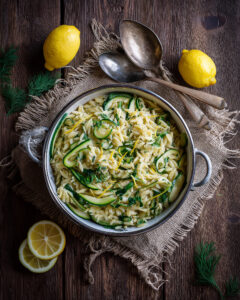 Lemon herb spring vegetable orzo with zucchini, fresh herbs, and lemon zest in a serving bowl on a rustic wooden table