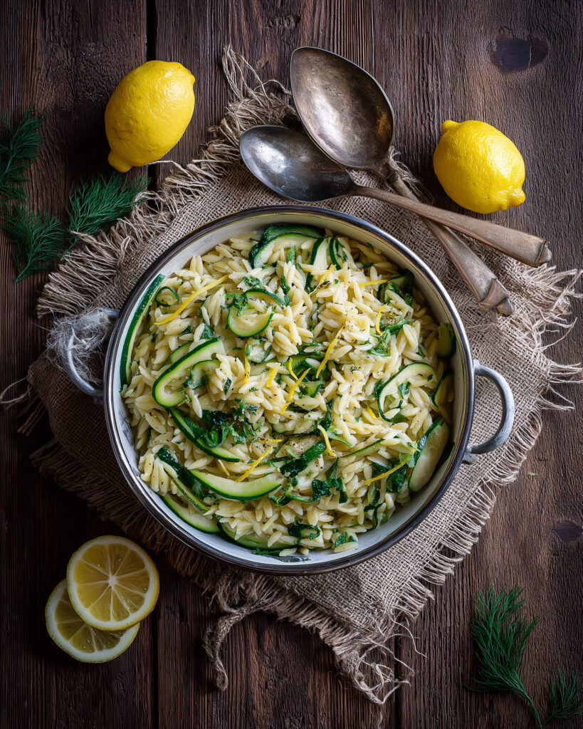 Lemon herb spring vegetable orzo with zucchini, fresh herbs, and lemon zest in a serving bowl on a rustic wooden table